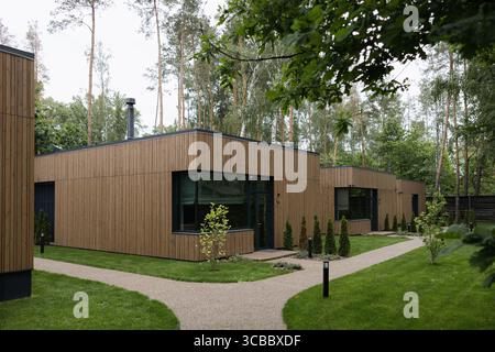 Modernes Holzhaus mit großen Fenstern und minimalistischem Design, umgeben von Bäumen und grüner Landschaft Stockfoto