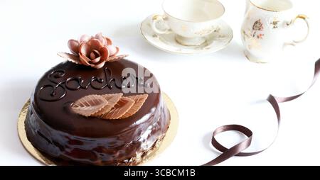Ganze Sachertorte (Schokoladen-sacher-Kuchen). Berühmtes traditionelles österreichisches Dessert. Tassen Kaffee in defokussierter Umgebung auf Hintergrund. Direkt darüber. Stockfoto