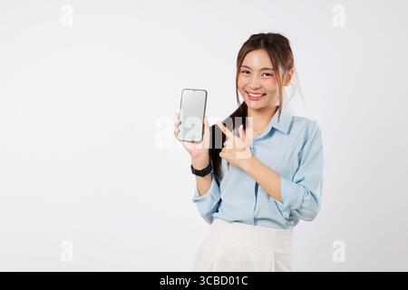 Eine glückliche asiatische Frau zeigt ihr Handy und zeigt mit dem Finger auf das Display Stockfoto