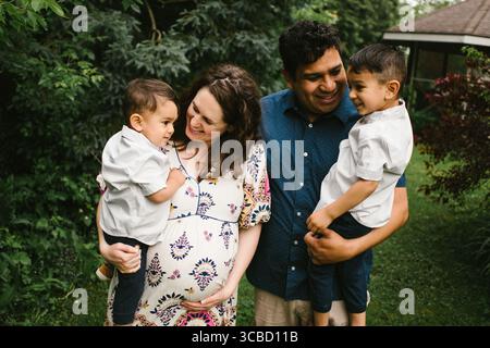 Schwangere Mutter mit Mann und zwei Kindern zusammen glücklich und lächelnd Stockfoto