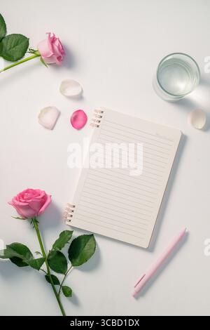 Elegante rosafarbene Rosen mit Notizblock und Stift Stockfoto