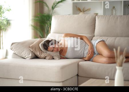 Frau mit prämenstruellem Syndrom, die auf einer Couch liegt und sich zu Hause beschwert Stockfoto