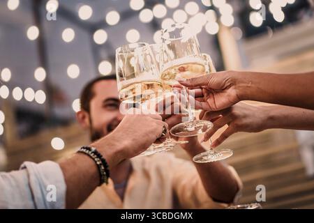 Nahaufnahme von Freunden, die bei einem feierlichen Toast mit Sekt oder Champagner Gläser anstoßen. Eine festliche Partyszene am Abend mit wunderschönem goldenen Bock Stockfoto