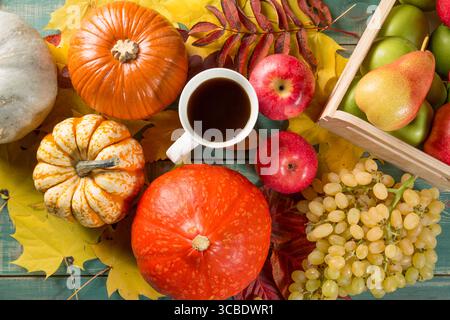 Reife Äpfel in einer Schachtel mit Kürbissen, Äpfeln, Trauben, Birnen und einer Tasse Kaffee auf grünem hölzernem Hintergrund. Jahreszeitbild Herbst. Draufsicht. Stockfoto