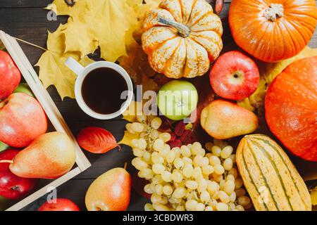 Reife Äpfel in einer Schachtel mit Kürbissen, Äpfeln, Trauben, Birnen und einer Tasse Kaffee auf dunklem hölzernem Hintergrund. Jahreszeitbild Herbst. Draufsicht. Stockfoto
