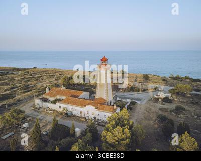 Blick aus der Vogelperspektive auf den leuchtend weißen Leuchtturm mit seiner leuchtenden roten Spitze, der stolz auf das ruhige blaue Meer und den Himmel steht, Leucate, Occitanie, Frankreich. Stockfoto