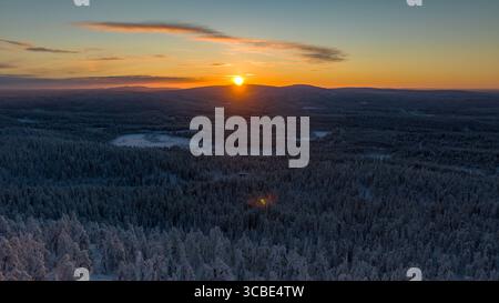 Aus der Vogelperspektive auf den Sonnenaufgang über schneebedeckten Wäldern und Hügeln, die einen goldenen Glanz über die Winterlandschaft ausstrahlen, Salla, Lappland, Finnland. Stockfoto