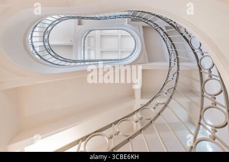 Elegante Wendeltreppe mit kunstvollem Metallgeländer in einem klassischen Gebäude. Architektonische Schönheit, geschwungene Stufen, Innenarchitektur, geometrisches Muster Stockfoto