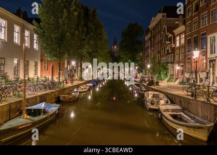 Nächtlicher Blick auf einen ruhigen Kanal gesäumt von Bäumen und Booten in Amsterdam, der das Wesen der niederländischen Architektur und der städtischen Ruhe einfängt Stockfoto