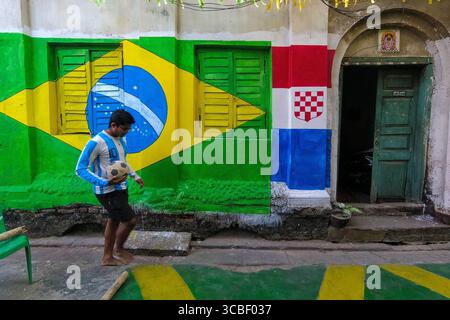 20. November 2022, Kolkata, Westbengalen, Indien: Ein Junge, der ein argentinisches Trikot trägt, geht an einer brasilianischen Flagge vorbei, die auf einer Wand gemalt ist, an einer Straße in Kalkutta, Indien , am 20. November 2022 (Bild: © Debarchan Chatterjee/ZUMA Press Wire) Stockfoto