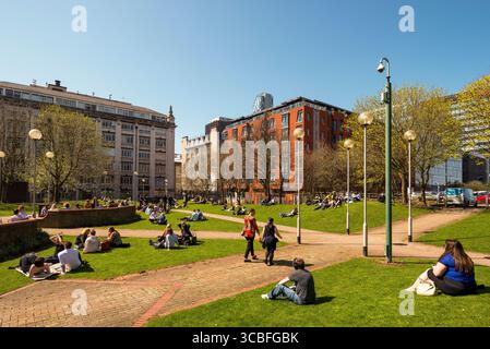 In einem sonnigen Stadtpark im Stadtzentrum von Liverpool, umgeben von historischer und moderner Architektur, entspannen und sich unterhalten. Stockfoto
