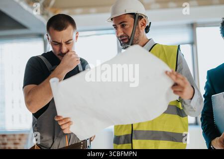 Zwei Bauexperten untersuchen Pläne und diskutieren Pläne in einem modernen Gebäude im Bau Stockfoto