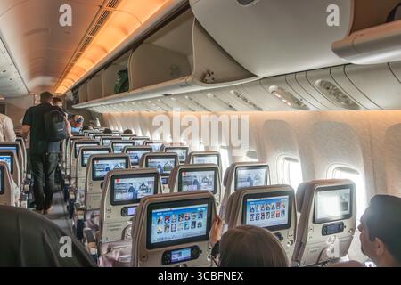 Innenansicht einer Economy Class-Kabine der Emirates Boeing 777 mit Passagieren, die sich an Bord der Flugbesatzung begeben, und Unterhaltungsbildschirme in der Rückenlehne sind sichtbar Stockfoto
