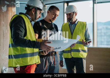 Das Bauteam bespricht die Baupläne vor Ort und trägt Sicherheitswesten Stockfoto