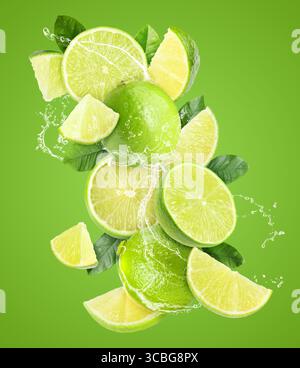 Frische Limetten und Spritzwasser in der Luft vor grünem Hintergrund Stockfoto