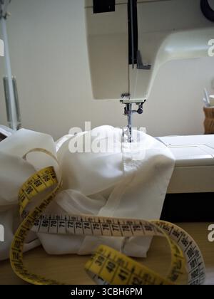 Industrielle Nähmaschine zum Nähen von weißem Stoff mit Maßband, Schneiderei und Details zur Bekleidungsherstellung. Stockfoto