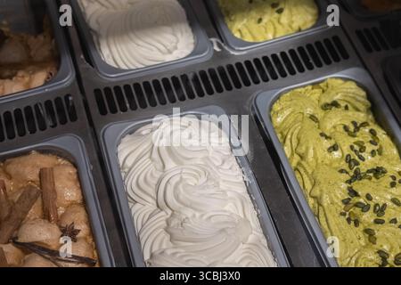 Verschiedene Eissorten in Tabletts, die in einem Geschäft ausgestellt werden. Creme, Pistazien, Kaffee Stockfoto