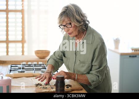 Eine ältere Frau, die Kekse in einer modernen Küche macht Stockfoto