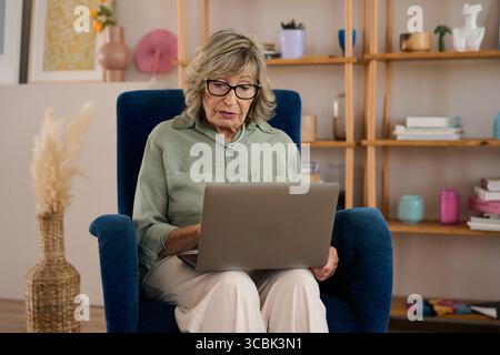 Zielgerichtete Seniorin, die zu Hause ein Notebook benutzt Stockfoto
