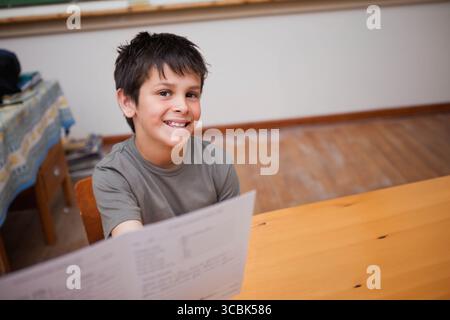 Junge Kind präsentiert Arbeitsblatt am Schreibtisch im Arbeitsbereich mit Beistelltisch mit Büchern, Kopierraum. Bildung, Unterricht, Lernen, akademisch, Jugend, che Stockfoto