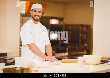 Männlicher Bäcker mit weißem, gleichmäßigem Knetteig auf bemehlter Arbeitsplatte in der Bäckerei mit Nudelnadel. Gebäck, Küche, Kunsthandwerk, Edelstahl, Kunsthandwerk Stockfoto