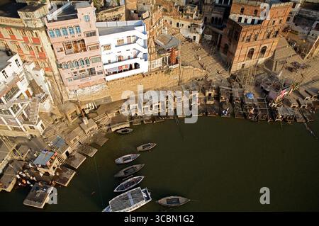 Aus der Vogelperspektive auf Booten, die sanft auf dem Ganges schweben, spiegeln die Erdtöne der alten Gebäude und Ghats am Flussufer, Varanasi, Uttar Pradesh, Indien wider. Stockfoto