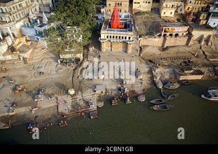 Blick aus der Vogelperspektive auf die lebendigen Gathats und Tempel entlang des heiligen Ganges, in warmes Licht getaucht, mit Booten auf dem Wasser, Varanasi, Uttar Pradesh, Indien. Stockfoto