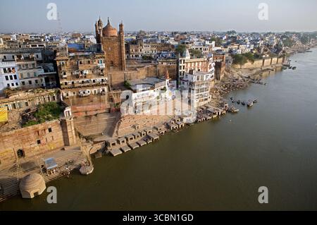 Aus der Vogelperspektive auf die Ghats der antiken Stadt, die zum Ganges River, einem Wandteppich aus ockerfarbenen Gebäuden unter einem trüben Himmel, Varanasi, Uttar Pradesh, Indien. Stockfoto