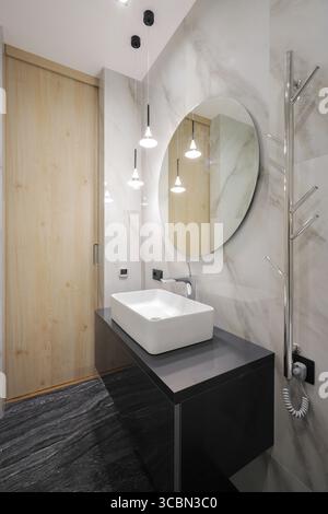 Wasserhahn mit Keramikwaschbecken und rundem Spiegel im Badezimmer Stockfoto