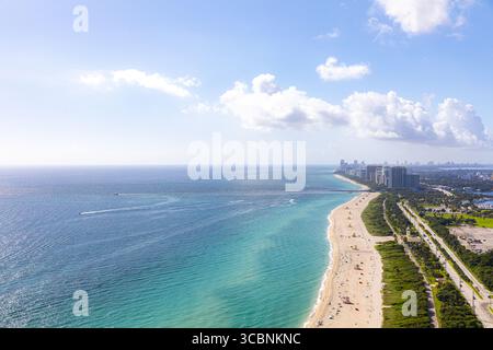 Blick aus der Vogelperspektive auf das türkisfarbene Wasser des Atlantischen Ozeans und den goldenen Sand entlang der Küste von Hallandale Beach, mit modernen Gebäuden, die sich am Horizont erheben, und einer parallel verlaufenden Straße, Surfside, Florida, USA. Stockfoto