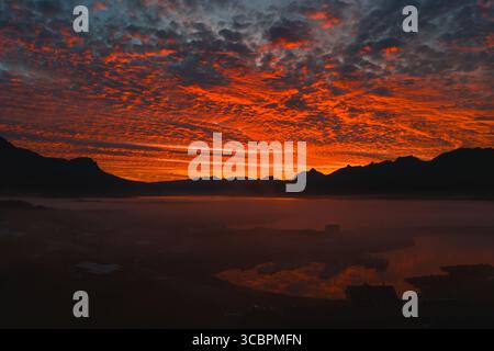 Feuriger Sonnenuntergang über isländischen Bergen und ruhigen reflektierenden Gewässern Stockfoto