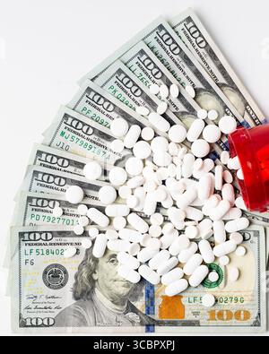 Verschreibungspflichtige Pille Flasche kippte mit Tabletten, die über gefächerte hundert Dollar Scheine auf weißem Hintergrund verschüttet wurden, symbolisieren steigende medizinische Kosten Stockfoto