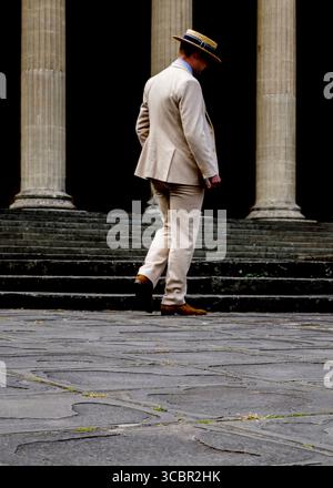 Ein Mann in hellem Anzug und Strohhut geht eine Treppe vor einem Gebäude mit großen Säulen hinunter. Stockfoto