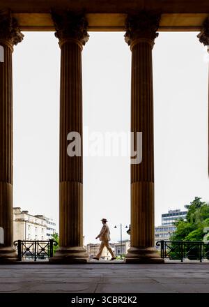 Ein Mann in Anzug und Hut läuft zwischen großen Säulen. Stockfoto