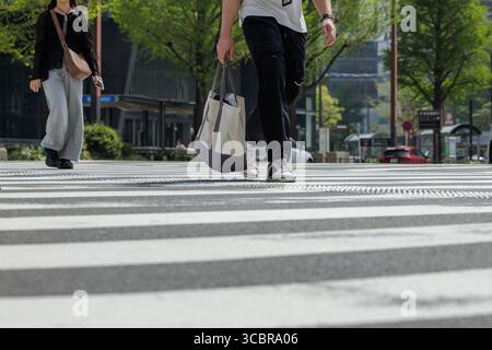 Fußgängerüberquerung mit flachem Blickwinkel. Zwei junge Menschen, die in stilvoller Freizeitkleidung gekleidet sind, kreuzen große Kreuzungen mit weißen Zebralinien. Stockfoto