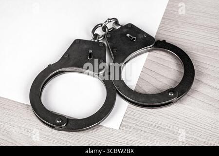 Handschellen und leeres Papier auf dem Tisch Nahaufnahme Stockfoto