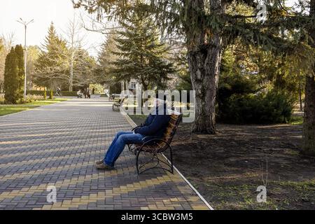 Ein älterer Mann mit Gesichtsmaske sitzt während der Pandemie auf einer Bank im Herbstpark. Der Begriff des Gesundheitsschutzes. Kopierbereich Stockfoto