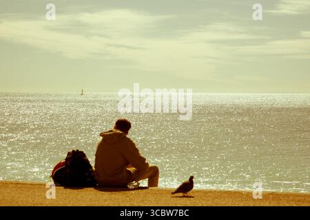 Unfokussierte Person, die am Strand sitzt und in die Ferne blickt Stockfoto