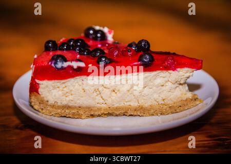 Ein Stück Käsekuchen mit schwarzen Johannisbeeren auf einem Tisch auf einem weißen Teller. Stockfoto