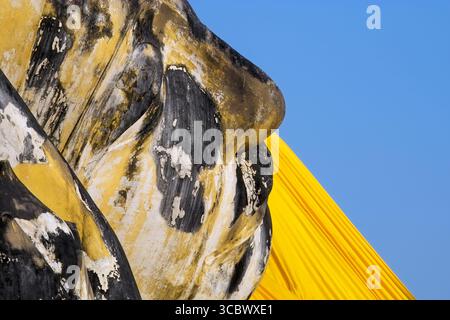 Nahaufnahme des Gesichts eines verwitterten Buddhas mit alter Textur, heiterem Ausdruck und zeitloser spiritueller Präsenz in Stein oder Metall. Stockfoto