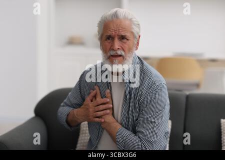 Ein älterer Mann, der zu Hause an Brustschmerzen leidet Stockfoto