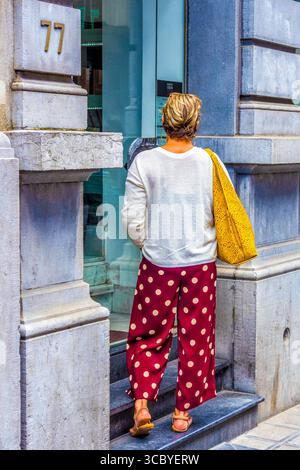 Rückansicht einer jungen Frau in Pünktchenhosen, die in der Tür steht - Brüssel, Belgioum. Stockfoto