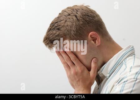 Trauriger müder Mann, der das Gesicht mit der Hand auf hellem Hintergrund bedeckt. Leerzeichen für Text Stockfoto