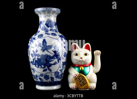 Blau-weiße orientalische Vase mit weißer Maneki Neko winkender Glückskatze isoliert auf schwarzem Hintergrund Stockfoto