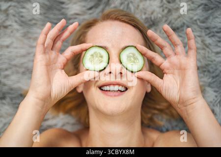 Eine junge Frau, die Gurkenscheiben für die Schönheitsbehandlung auf die Augen aufträgt Stockfoto