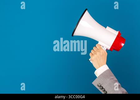 Weibliche Hand in Business-Anzug oder Jacke mit Lautsprecher-Megaphon vor blauem Hintergrund. Stockfoto