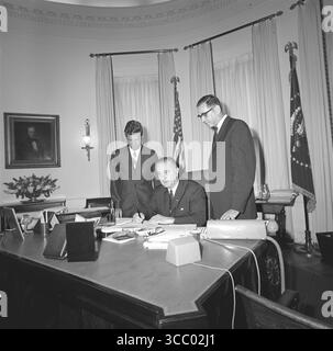Präsident Lyndon B. Johnson unterschreibt eine Gesetzesvorlage im Oval Office, während die Mitarbeiter zusehen Stockfoto