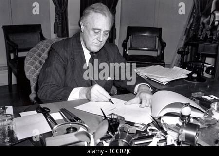 Präsident Franklin D. Roosevelt, halblanges Porträt, sitzt am Schreibtisch, schaut nach unten, unterschreibt H.R. 1776. das Lend-Pacht-Gesetz, um Großbritannien, China und Griechenland zu helfen. Stockfoto