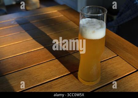 Ein erfrischendes Glas leichtes Bier mit einem schaumigen Kopf auf einem Holztisch 3 Stockfoto