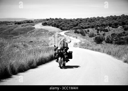 Schwarz-weißes Motorrad, das durch die Landschaft Siziliens, Italien, fährt Stockfoto